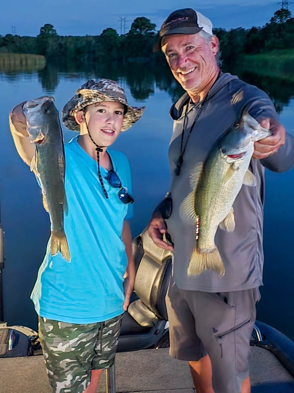 Guide and young angler with two largemouth bass at dusk on Lake Bastrop