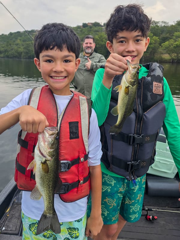 Two young anglers each holding a largemouth bass with Dad approving in the background